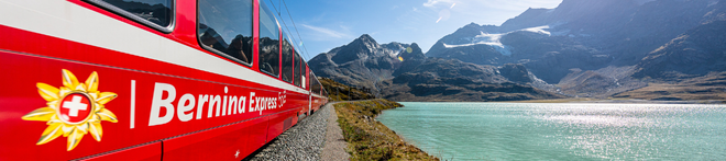Red Bernina Express train traveling along a turquoise lake with majestic mountains under a clear blue sky in the background.