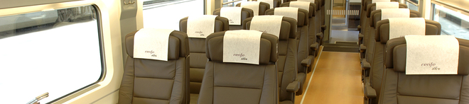 Rows of empty, modern train seats with brown upholstery and white headrest covers, situated by large windows on both sides.