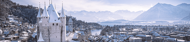 Snow-covered castle and town with mountains in the background under a clear blue sky.