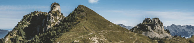Panoramic view of a mountainous landscape with rugged peaks, grassy slopes, and clear blue sky.